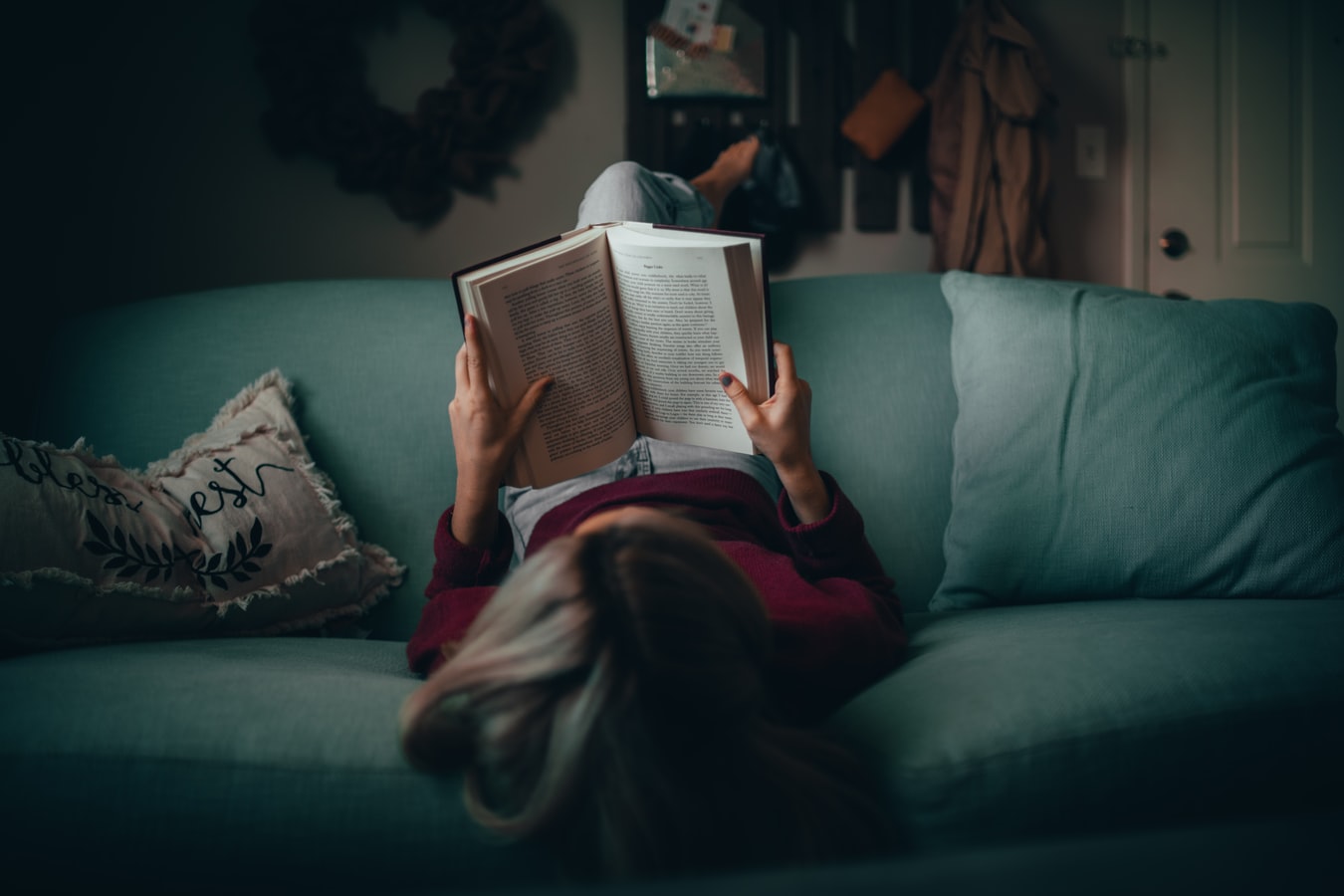 woman laying backwards on couch reading a book