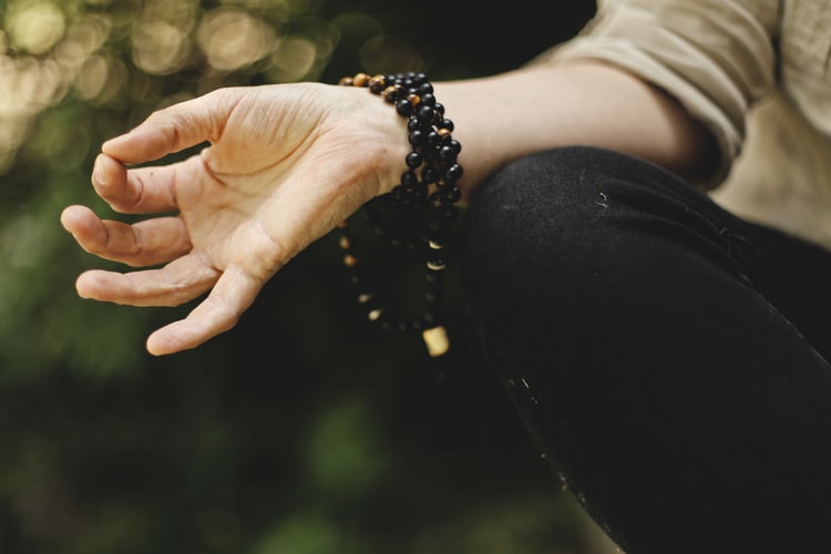 woman meditating with beaded bracelet