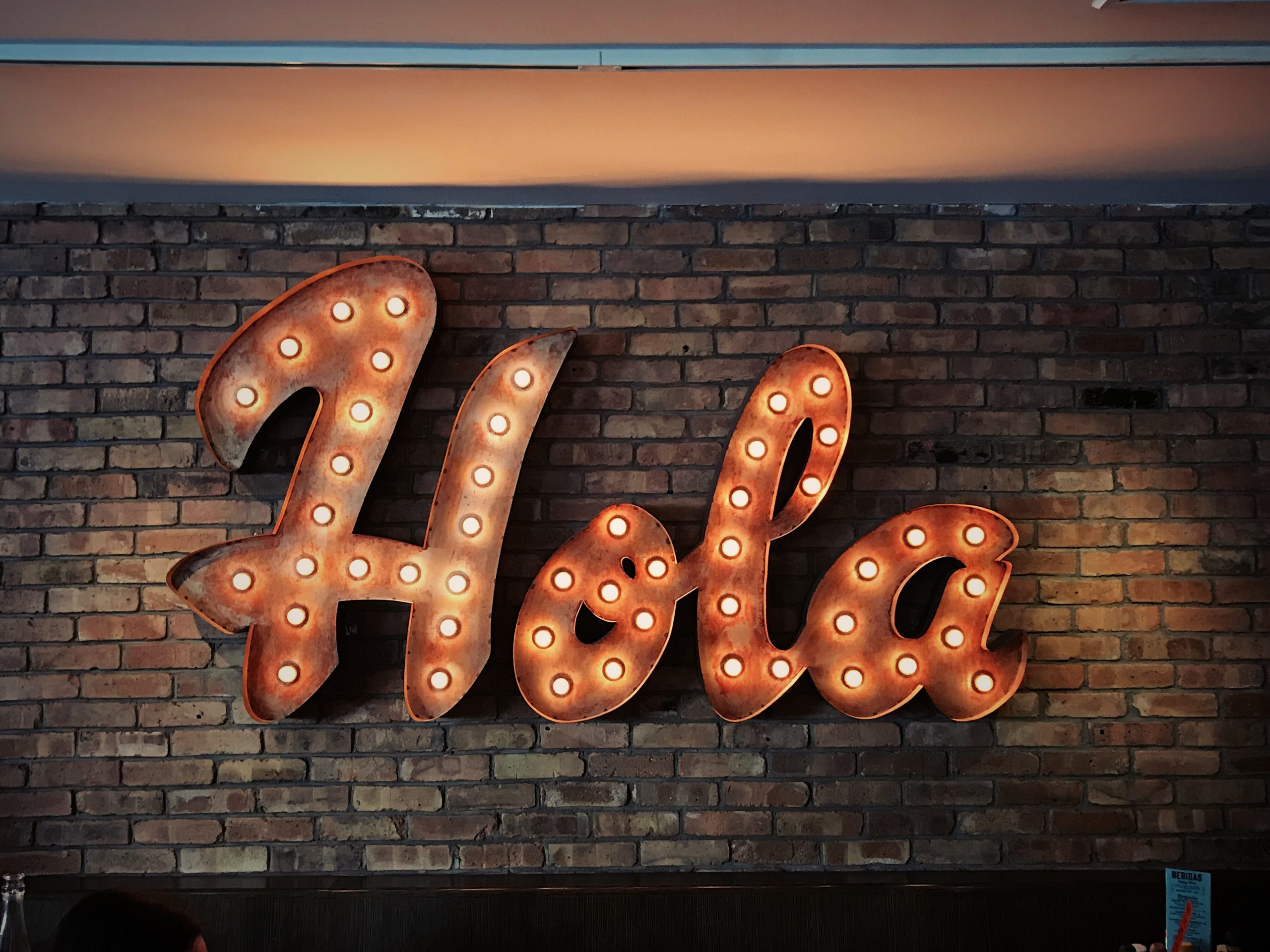 hola in neon sign on a brick wall
