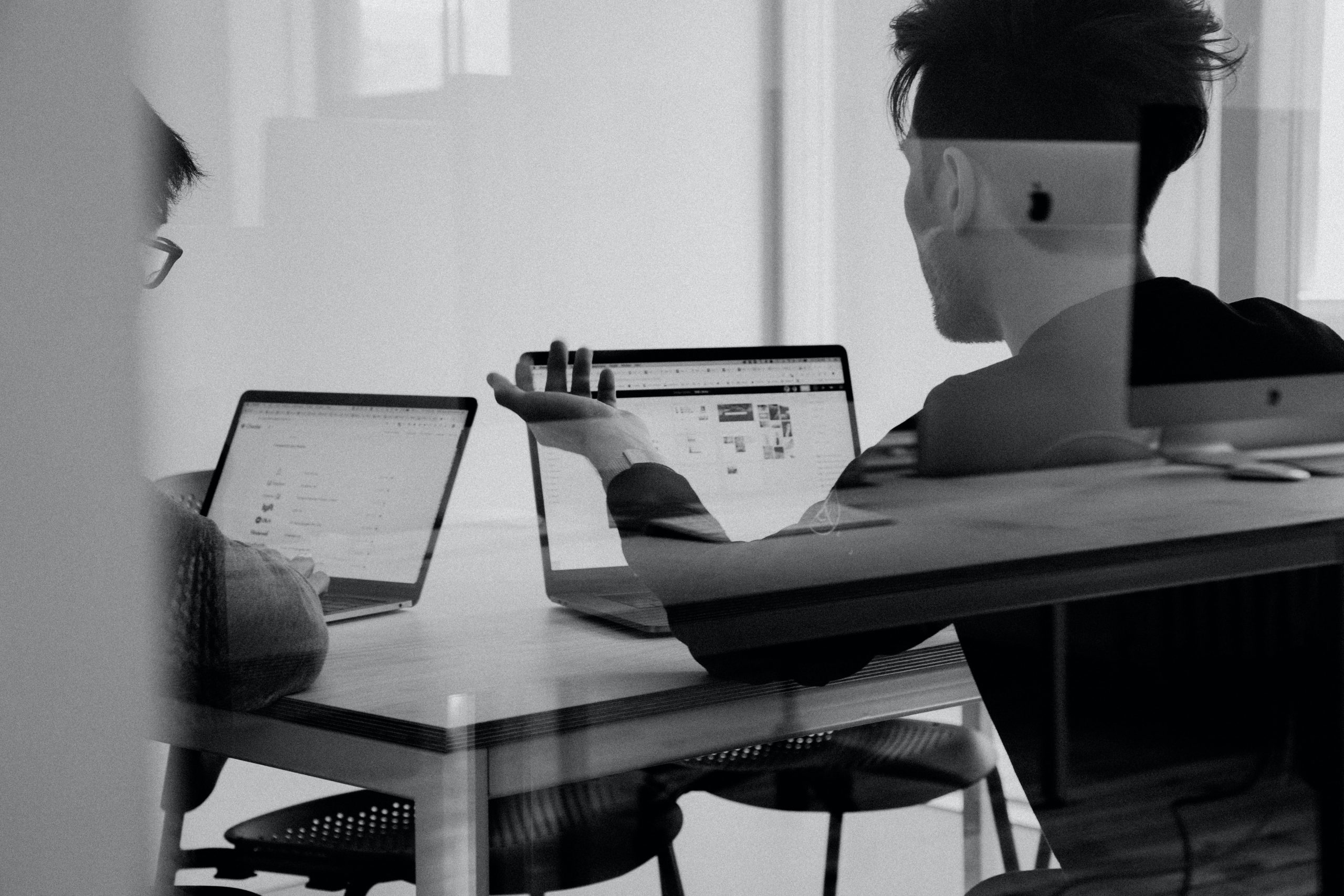 black and white photo of people working on laptops talking