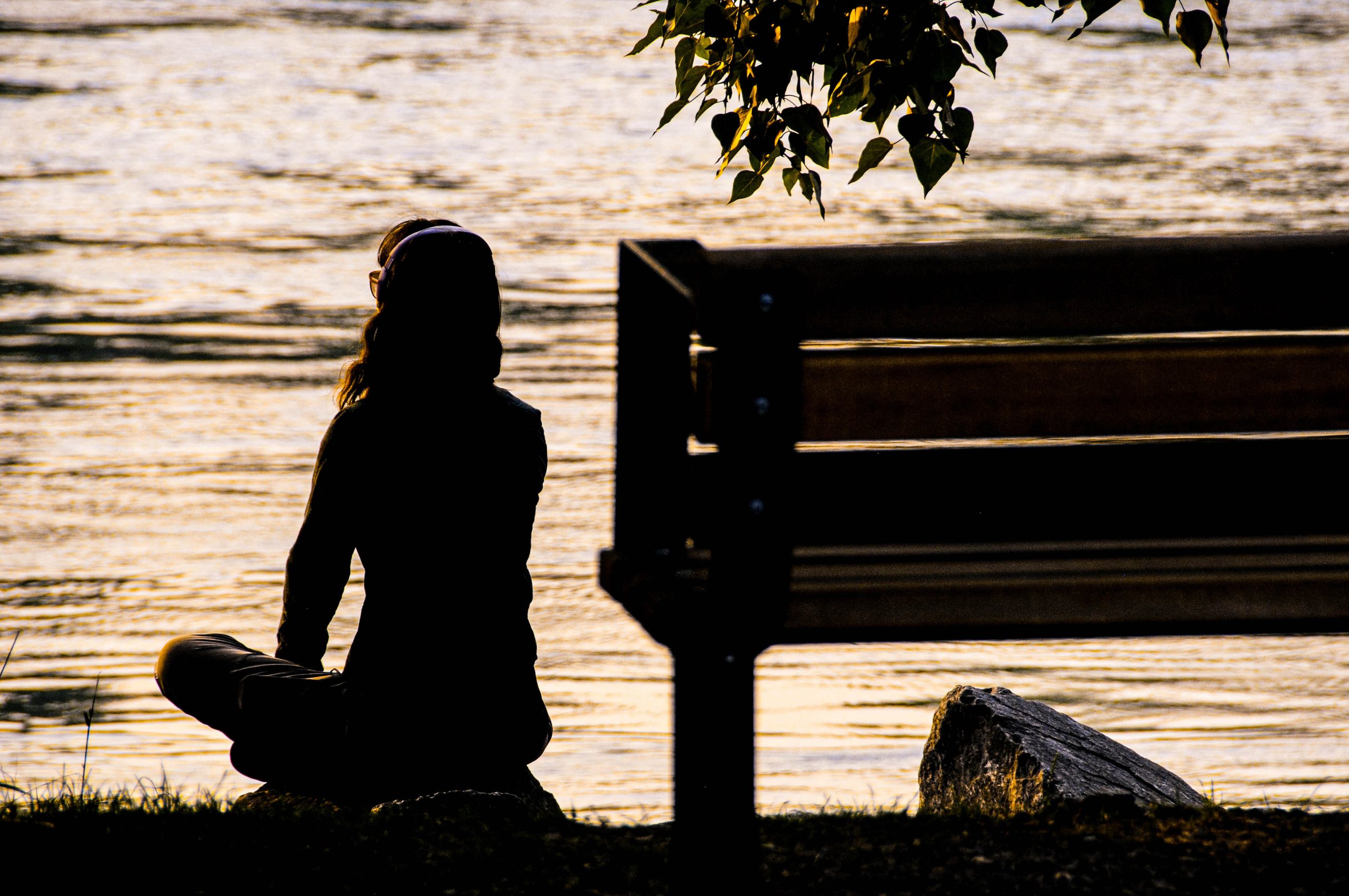 silhouette of woman sitting beside a bench, meditating