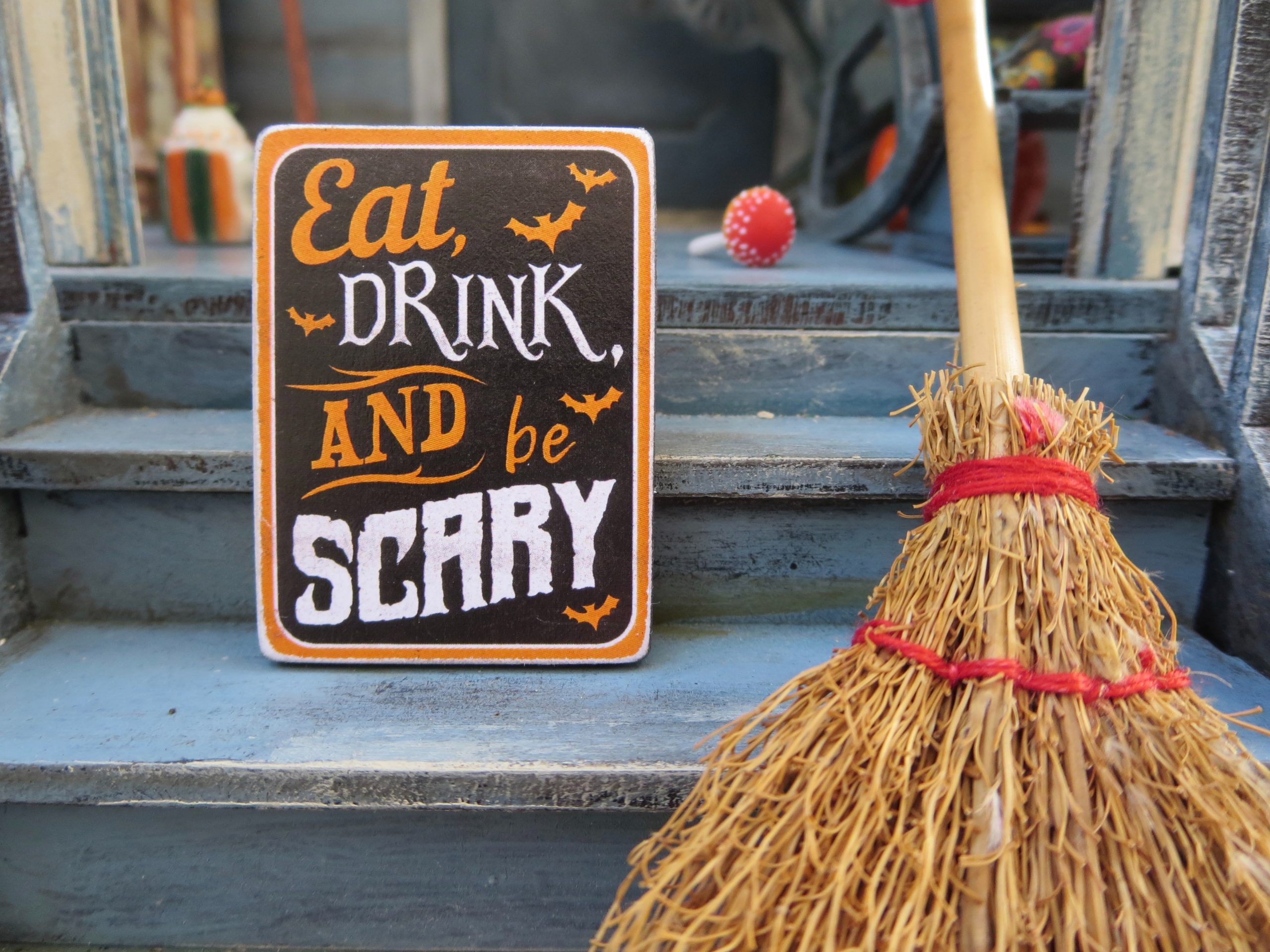 sign with a wooden broom that reads 'eat drink and be scary'