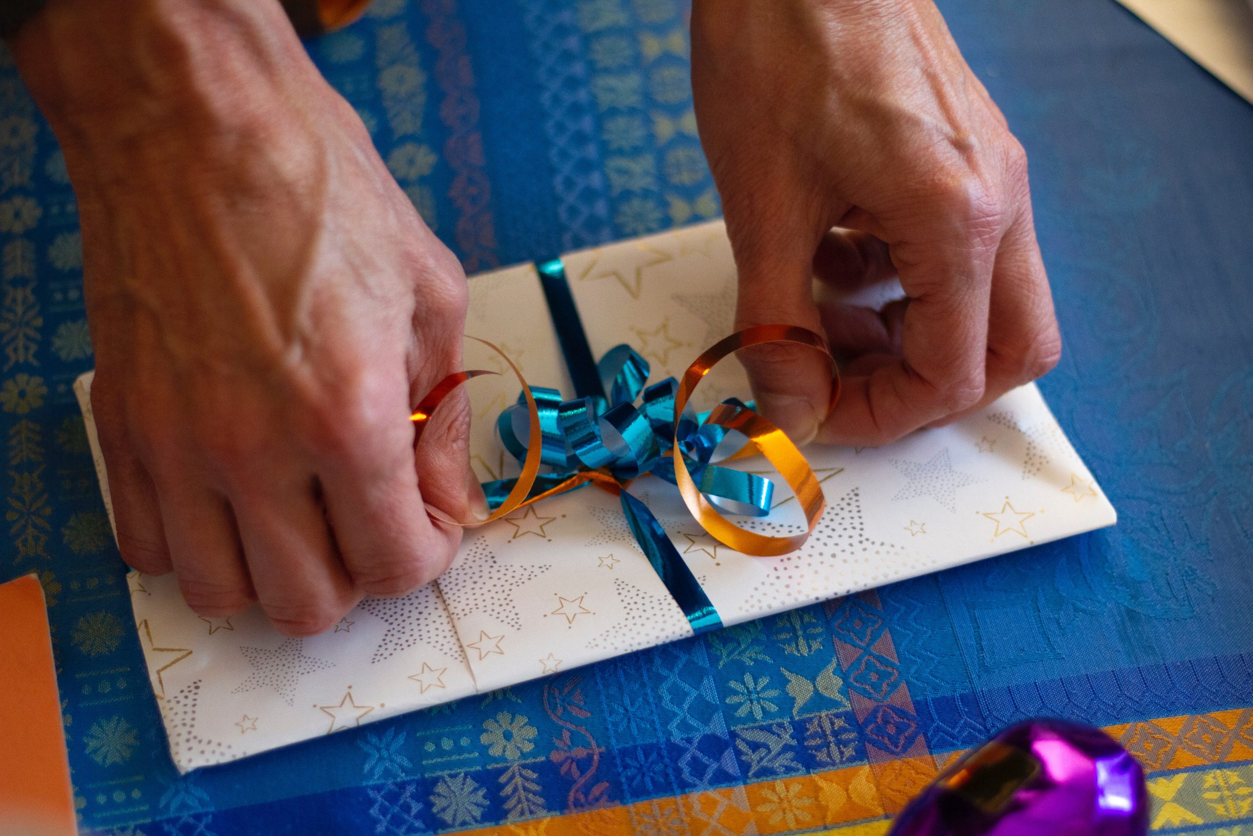 hands tying a blue and orange ribbon on a present