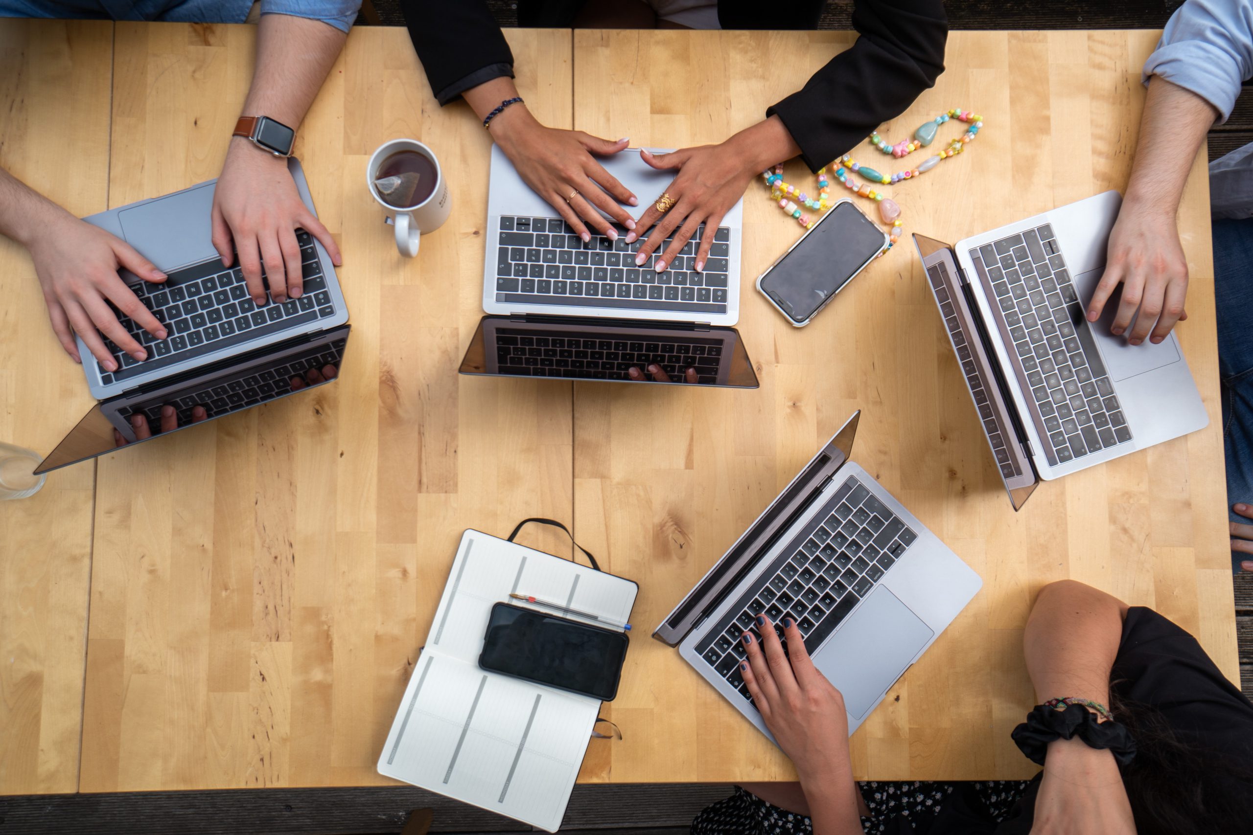 Aerial view of open work laptops and hands around a wooden table